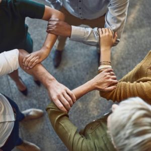 High angle shot of a group of colleagues linking arms in solidarity at work